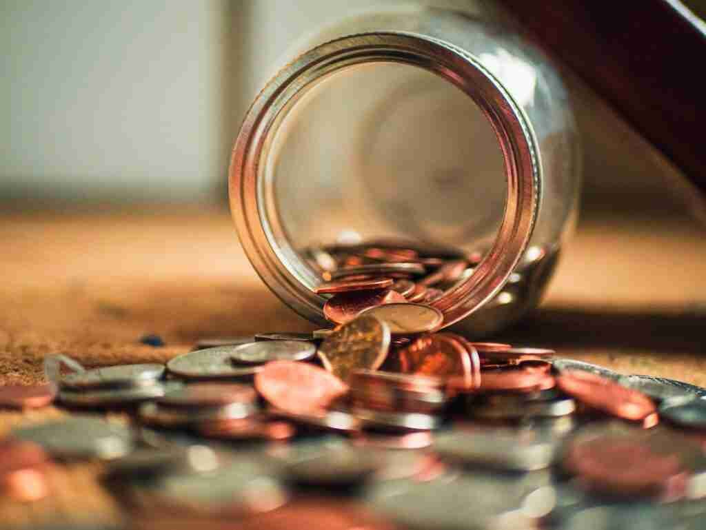 Coins spilling out from an overturned glass jar onto a wooden surface, symbolizing easy ways to Get Money in Your Bank Account Now Free.