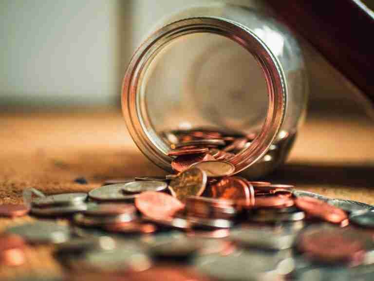 Coins spilling out from an overturned glass jar onto a wooden surface, symbolizing easy ways to Get Money in Your Bank Account Now Free.