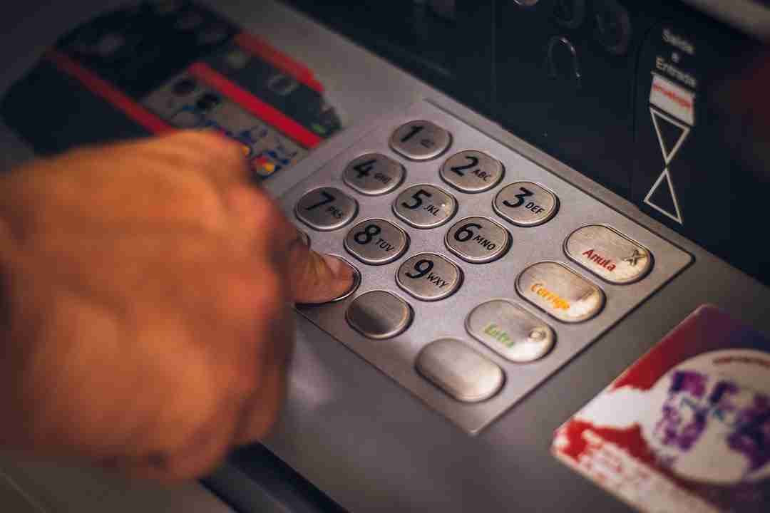 A person pressing the number 5 on an atm keypad to carry out a transaction related to their UK bank account for non-residents.